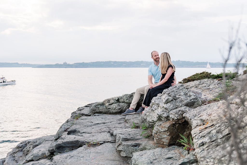 couple sits on rocks after engagement at castle hill