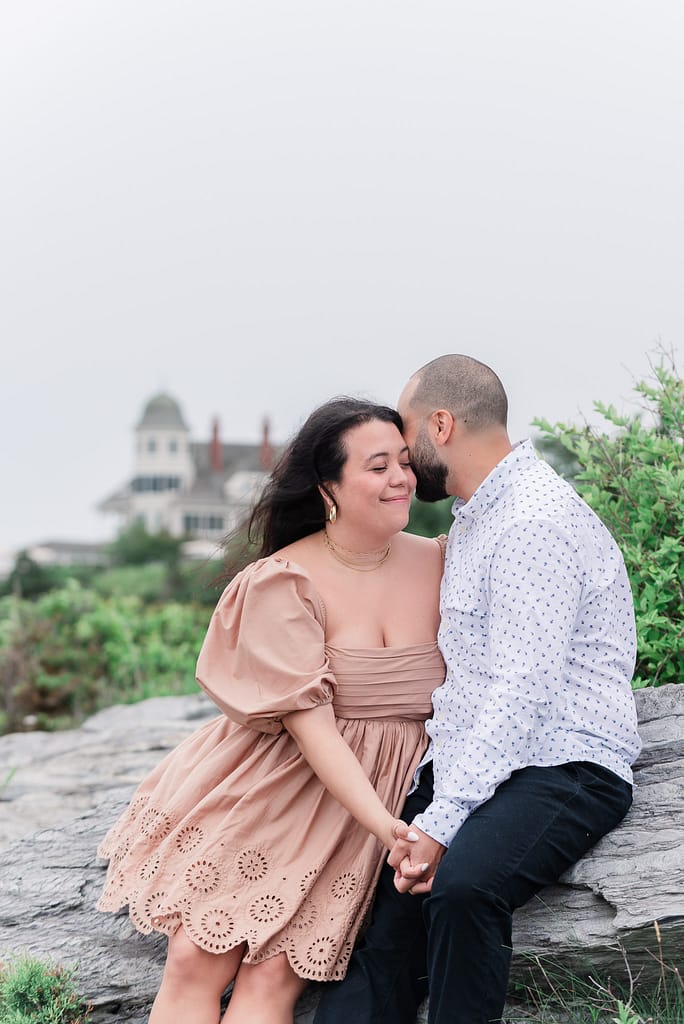 couple sits on rock at castle hill after rhode island surprise engagement