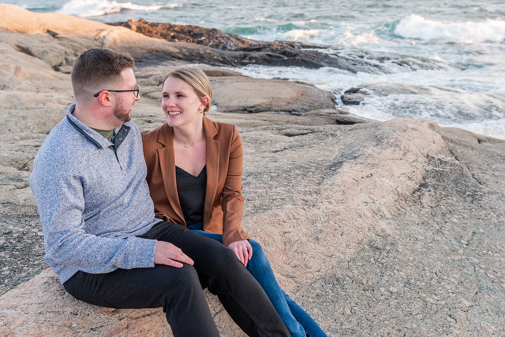couple sits on rocks after proposal at ledge road on cliff walk